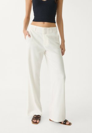 White, high-waisted, wide-leg pants with a smooth texture and side pockets, paired with a dark cropped knitted top and brown sandals.