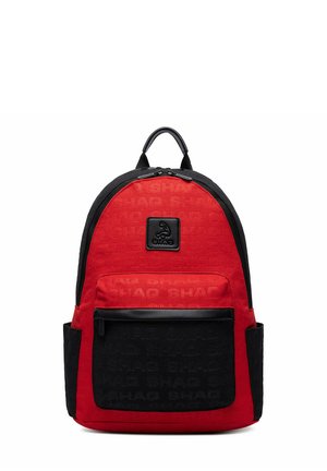 Roter und schwarzer Rucksack mit vorderer Reißverschlusstasche, Seitentaschen, oberem Griff und einem Logo-Patch mit einer kleinen Figur und Text "SHAG" vorne.