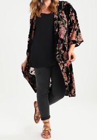 Black floral kimono with a velvet texture, featuring pink and green floral patterns, worn over a black top and gray jeans with brown sandals.