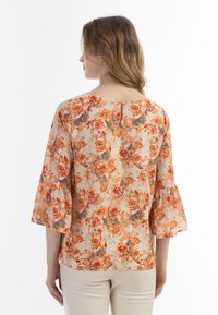 Blomstret bluse med orange og grå blomster på en cremet baggrund. Korte flagrende ærmer og en nøglehulskæring i ryggen med knapdetalje.