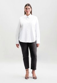 Wit overhemd met knopen, lange mouwen en een gestructureerde kraag, gecombineerd met donkergrijze aansluitende broek. Soepele stof, minimale details.