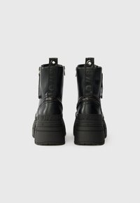 Par de botas chunky pretas com plataforma, com "BUFFALO" embutido no calcanhar e "LOVE/B" impresso nas alças, vistas de trás.