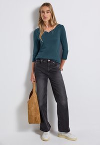 Haut bleu canard à manches longues avec un décolleté en V et des manches trois-quarts, associé à un jean large taille haute noir et des baskets blanches. Sac fourre-tout en cuir Suédé marron.