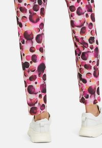 Multicolored trousers featuring a patterned design in shades of pink, purple, and orange, paired with white sneakers.