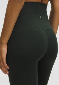 Spodnie do jogi w kolorze ciemnozielonym, wysokiej talii, wykonane z gładkiego, elastycznego materiału; mają logo z tyłu oraz dopasowany krój dla zapewnienia komfortu.