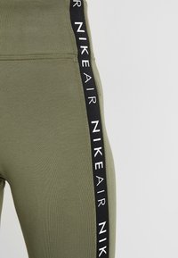 Vihreät leggingsit, joissa on sileä pinta, mustalla sivuraidalla, jossa on valkoinen "NIKE AIR" -teksti. Slim fit -muotoilu korostaa jalkaosan muotoa.