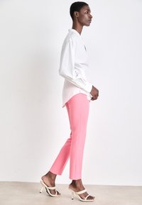 White long-sleeve shirt paired with bright pink fitted pants, featuring a sleek design. The model wears open-toed heels.