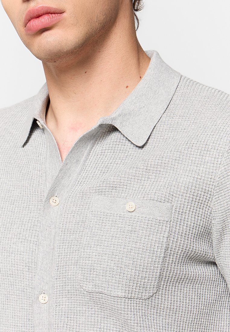 Grijs gemêleerd polo shirt met een subtiel ruitpatroon, korte kraag en een enkele borstzak met knoopsluiting.