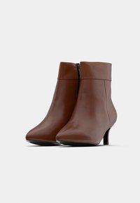 Ruske nahkasaapad nilkkoihin, joissa on terävä vaippa ja pieni korko. Siinä on sivuvetoketju ja sileä pinta, jossa on tyylikäs muotoilu.