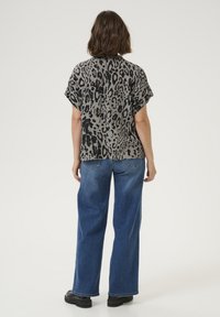 Haut à motifs léopard en gris avec des taches noires, à manches courtes et coupe décontractée, associé à un jeans en denim bleu à jambes larges et des bottes noires.
