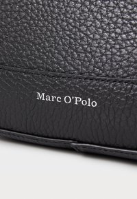 Zwarte leren tas met een gepolijste textuur. Voorzien van een gestikte naad en de merknaam "Marc O'Polo" in het wit geperst.