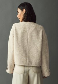 Textured beige sweater with a relaxed fit, drop shoulders, and long sleeves, paired with light beige high-waisted pants.