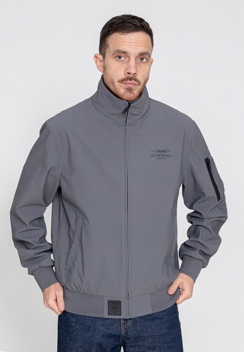 Graue Bomberjacke mit hohem Kragen, Reißverschlusstaschen und elastischen Bündchen. Merkmale ein Logo auf der Brust und eine feste Stofftextur.