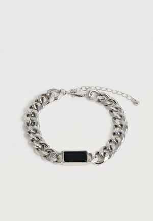 Silberner Kettenarmband mit schwarzer rechteckiger Platte und verstellbarem Verschluss auf hellem Hintergrund.