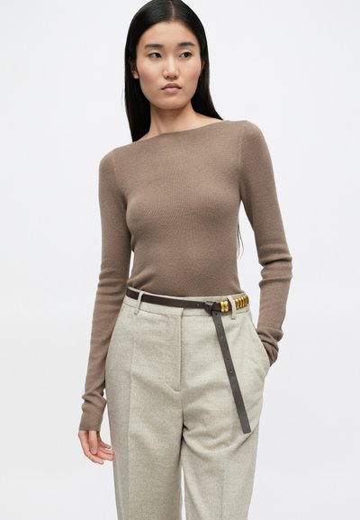 Brūna ribota ilga piedurkne top ar laivu kakla izgriezumu, apvienota ar gaiši pelēkiem pielāgotajiem biksēm un brūnu jostu ar zelta akcentiem.