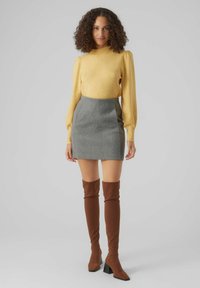 Yellow, fitted sweater with textured yarn; gray mini skirt with contrasting side panels; brown over-the-knee boots with block heels.