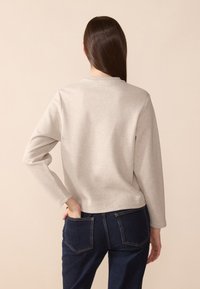 Sweat-shirt gris à manches longues, col rond et coupe décontractée, associé à un jean bleu foncé avec poches arrière. Texture de tissu lisse.