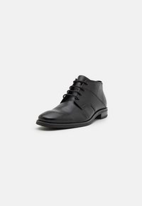 Botines de cuero negro con un acabado suave, punta redonda y diseño de cordones. Presentan detalles de costura y un tacón bajo.