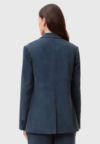 Blazer blu scuro in tessuto morbido, con una fessura singola sul retro, revers a punta e dettaglio a tre bottoni sui polsini.