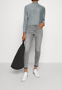 Knitted, light gray sweater with long sleeves, paired with gray skinny jeans. White sneakers and a black bag complete the look.