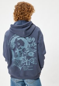 Granatowy hoodie z dużym nadrukiem na plecach, przedstawiającym elementy muzyczne i szczegóły festiwalu w jasnoniebieskim kolorze.
