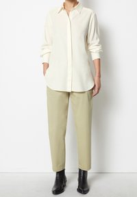 Crème-kleurig overhemd met kraag, gecombineerd met lichtgroene broek en zwarte enkellaarzen. Het overhemd heeft een losse pasvorm en de broek is licht getailleerd.