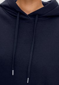 Mörkblå hoodies i mjukt tyg, med dragsko i huvan och silverfärgade metallspetsar, samt en slät yta utan mönster.