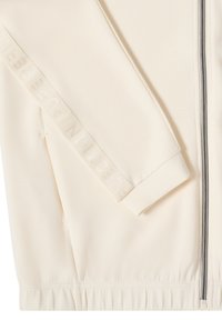 Chaqueta cremosa con cremallera y puños y dobladillo acanalados. Presenta texto reflectante a lo largo de la manga y una textura de tela suave y lisa.