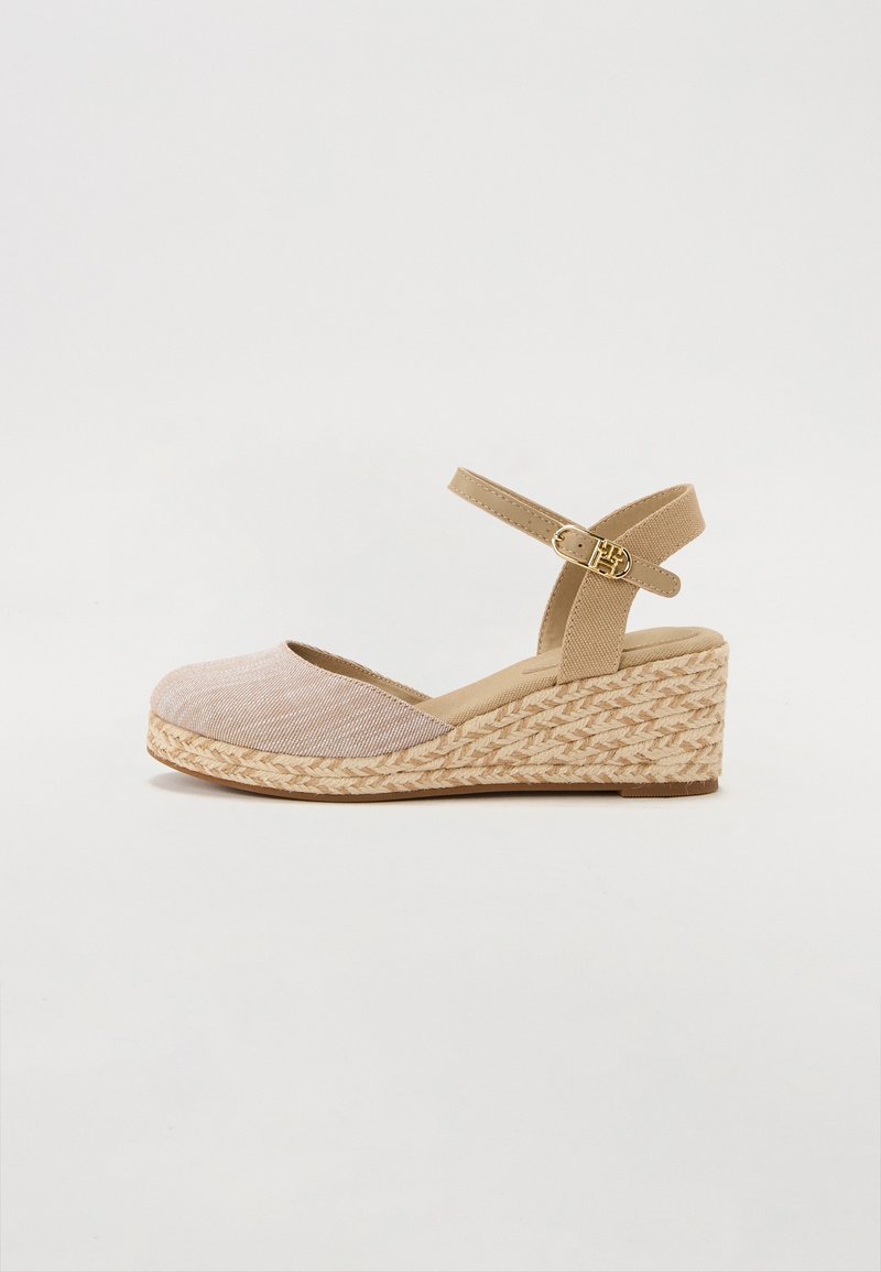 Sandale compensée beige avec plateforme en corde tressée, bout fermé et bride de cheville réglable avec boucle dorée sur un fond clair.