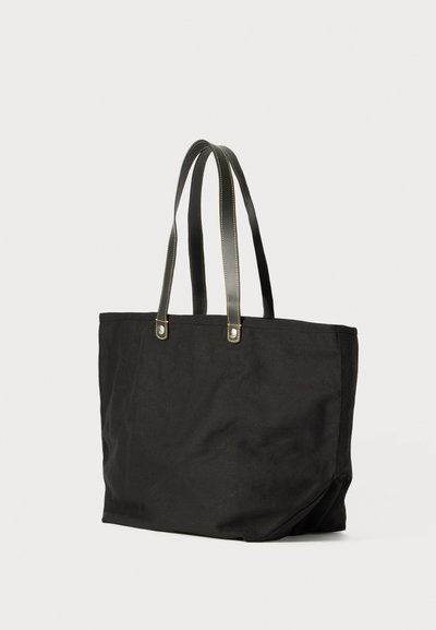 Borsa tote in tessuto nero con due manici in pelle nera, caratterizzata da cuciture gialle e un design spazioso e non strutturato.