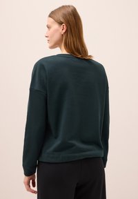 Mörkgrön sweatshirt i mjukt tyg, med rundad halsringning, hängande axlar och avslappnad passform. Enkel design utan synliga mönster.