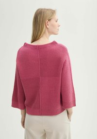 Maglione a maglia fucsia con texture a coste e scollo a barca ampio. Presenta maniche a tre quarti e una vestibilità rilassata, abbinato a pantaloni leggeri.