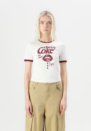 Balts īsais T-krekls ar bordo apdari, kas rotāts ar vintage stila "cherry Coke" grafiku un tekstu. Modelis valkā haki krāsas cargo bikses.