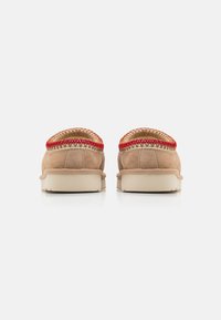 Beige suede kingad punaste õmblustega ümber krae, valge kummist tallaga ja minimalistliku disainiga. Tagantvaade toob esile õmbluste detaile.