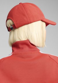 Röd basebollkeps med en texturerad tyg, med en böjd skärm och ett justerbart spänne bak, i kombination med en röd zip-up jacka.