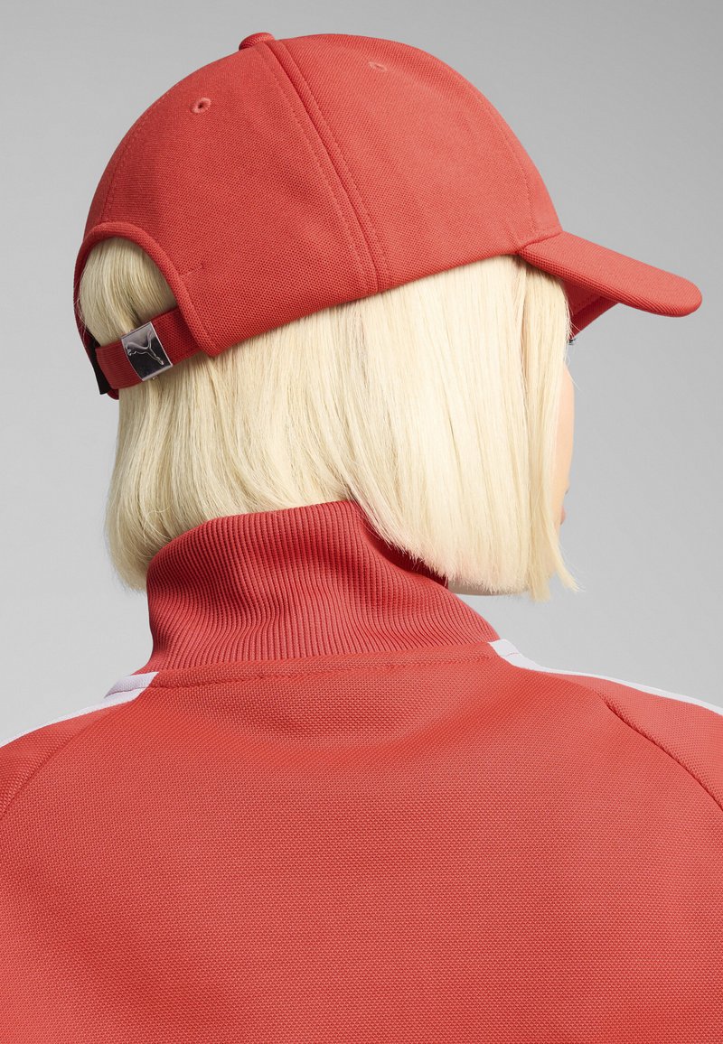 Röd basebollkeps med en texturerad tyg, med en böjd skärm och ett justerbart spänne bak, i kombination med en röd zip-up jacka.