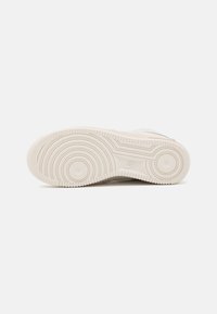 Nike sneaker sole in light beige, featuring circular tread patterns and smooth, textured accents. Slightly raised logo on side.