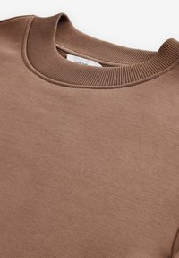 Sudadera marrón con cuello redondo acanalado, fabricada en un tejido suave. Presenta un diseño limpio y sencillo, sin patrones ni acentos.