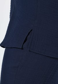 Tissu texturé bleu marine avec détail d'ouverture latérale sur vêtement superposé, mettant en valeur la couture et la texture du matériau.