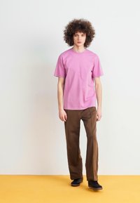 Rosa bomull t-skjorte med korte ermer, kombinert med brune rette bukser. Enkel design, ingen synlige mønstre eller detaljer.