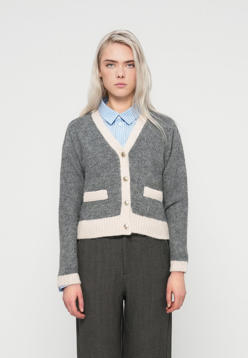 Gray and cream cropped cardigan with a V-neck, button front, and two patch pockets; ribbed hem and sleeve cuffs, soft texture.