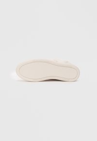 Cremefarbene Gummisohle mit strukturiertem Oberflächen, abgerundeter Kante und gemustertem Profil für guten Halt. Glattes, minimalistisches Design ohne sichtbare Markenkennzeichnung.