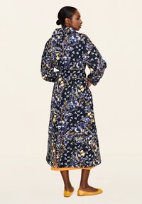 Langes florales Wickelkleid in Dunkelblau mit gelben und blauen Mustern; verfügt über einen Gürtel, lange Ärmel und einen kontrastierenden orangen Saum.
