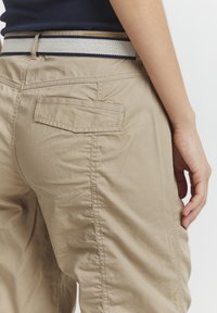Pantalons en tissu léger beiges avec une coupe décontractée, dotés d'une poche arrière et d'une ceinture tissée texturée multicolore.