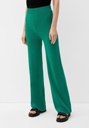 Pantalons larges verts en tissu lisse et léger. Dotés d'une taille élastique haute et d'un design sans ornements. Associés à des sandales noires.