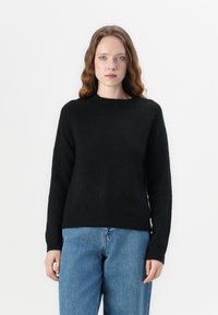 Svart stickad tröja med rund halsringning och långa ärmar, med en mjuk textur; matchas med ljusblå denimjeans.