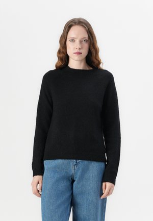Maglione nero in maglia con scollatura a girocollo e maniche lunghe, caratterizzato da una texture morbida; abbinato a jeans in denim blu chiaro.