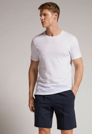 Witte katoenen t-shirt met korte mouwen, gecombineerd met marineblauwe katoenen shorts met zijzakken en een trekkoord in de taille.