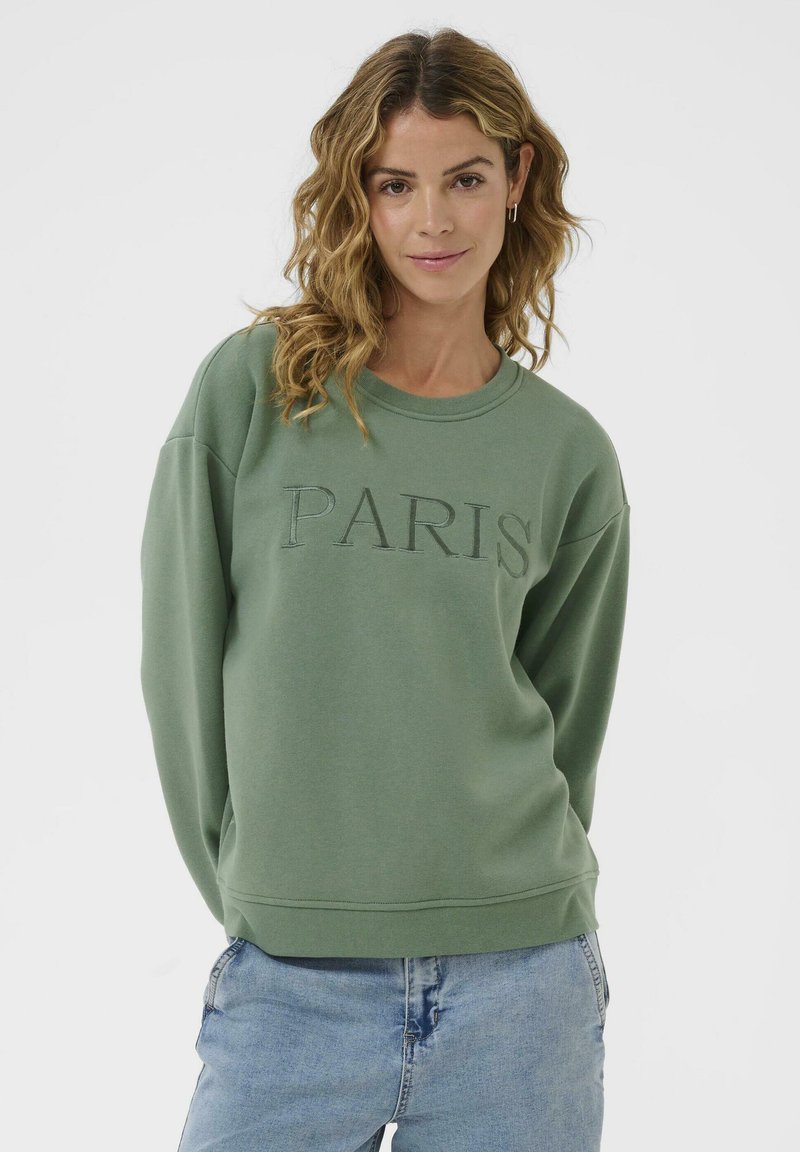 Sweatshirt vert avec "PARIS" brodé dans un fil assorti. Présente un col rond, des épaules tombantes et des poignets côtelés. Texture lisse.
