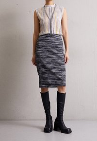 Šedá a černá pruhovaná midi sukně v kombinaci s vícebarevným topem bez rukávů. Celkový vzhled doplňují černé kozačky po kolena.